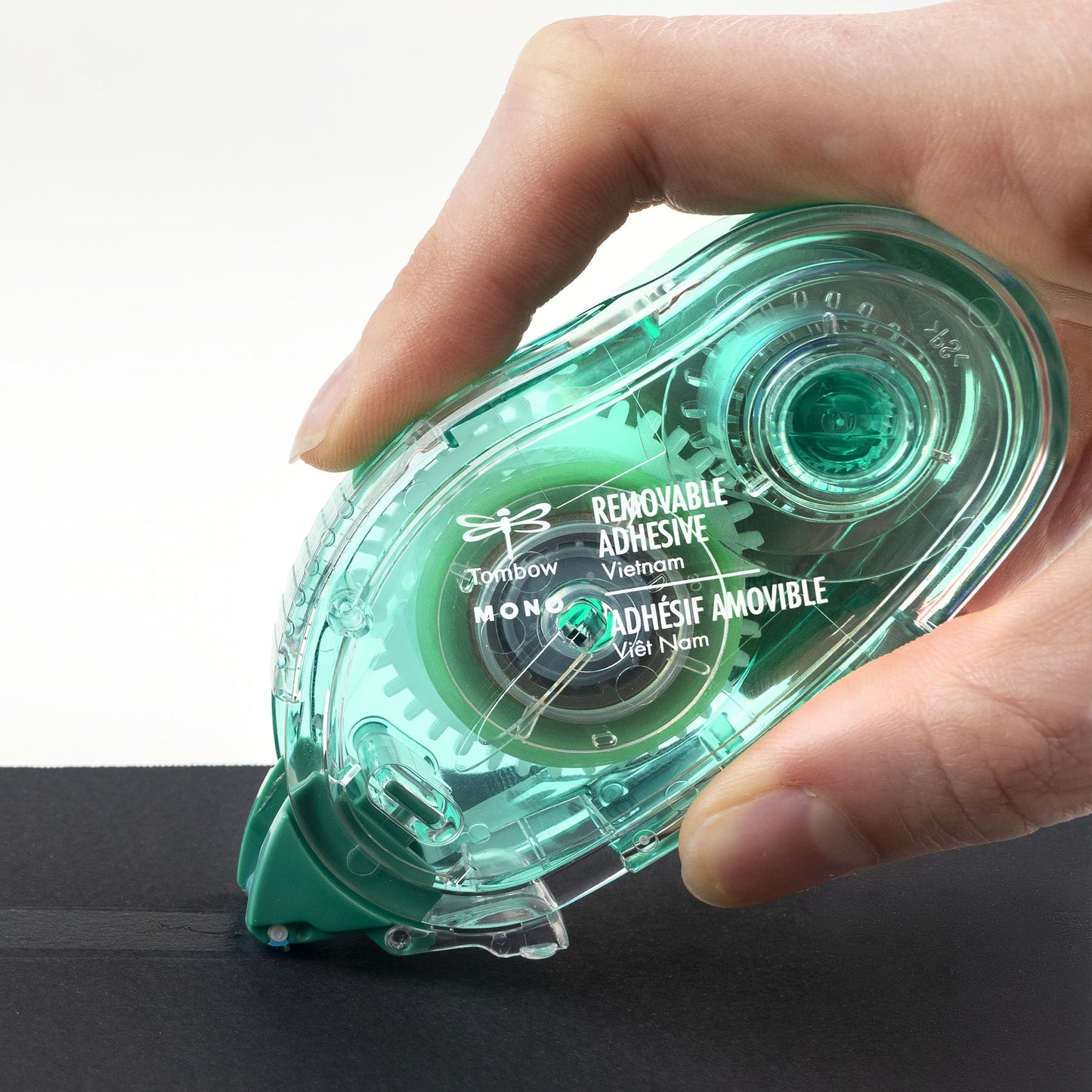 Hand holding a green removable adhesive tape dispenser against a white background