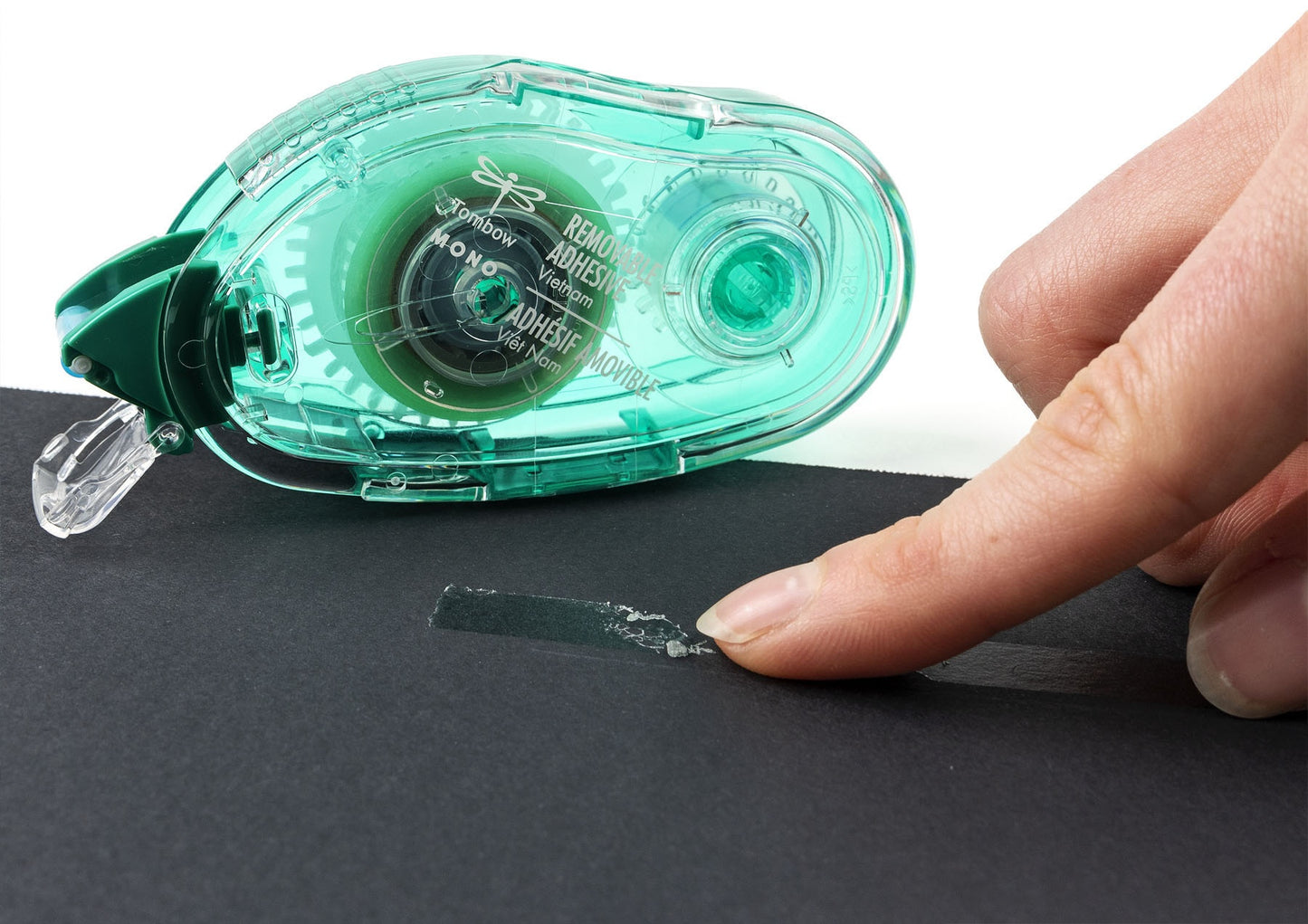 Green adhesive tape dispenser being used on a black surface