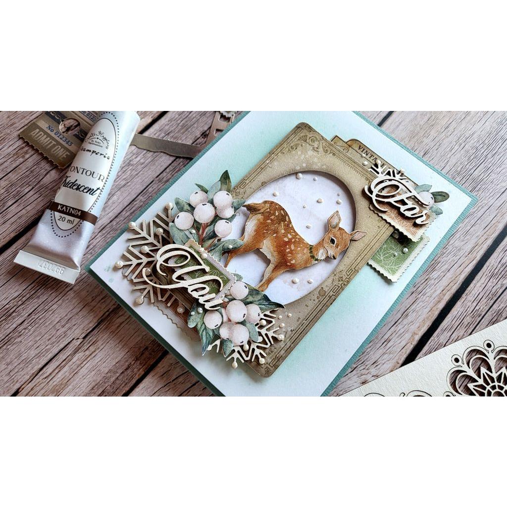 A handmade layered greeting card featuring a small deer, berries, and decorative script elements, styled on a rustic wooden surface with a tube of paint nearby.