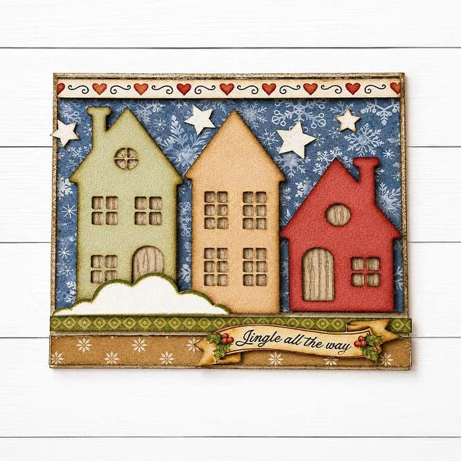 A handmade card featuring three stylized houses in beige, tan, and red, set against a blue snowy background with white stars. A banner at the bottom reads 'Jingle all the way' with small holly accents.